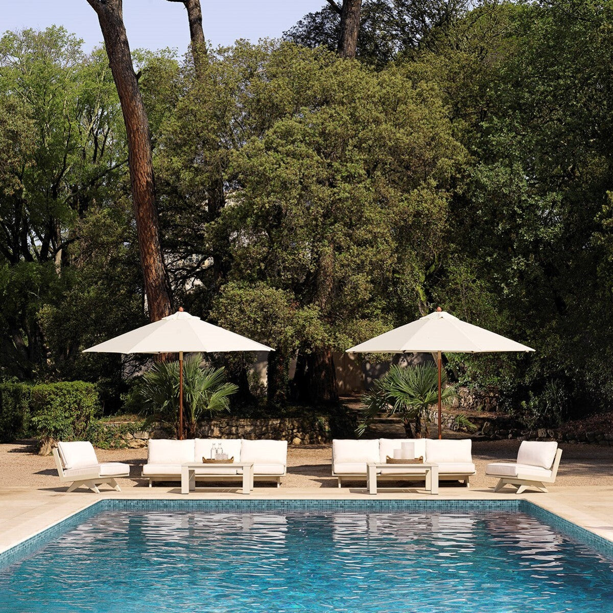 Elegant outdoor seating with umbrellas beside a serene pool in a lush green garden setting.