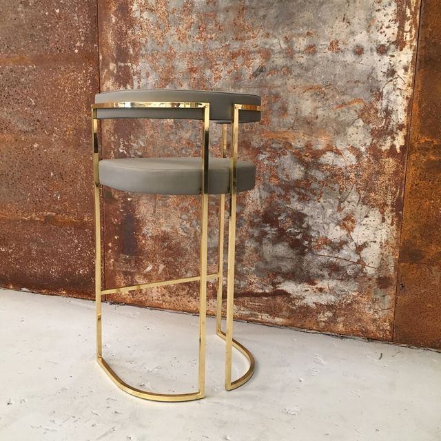 Julius Gri gold bar stool with fabric upholstery, sleek design on rustic background, height 101 cm, stylish seating.