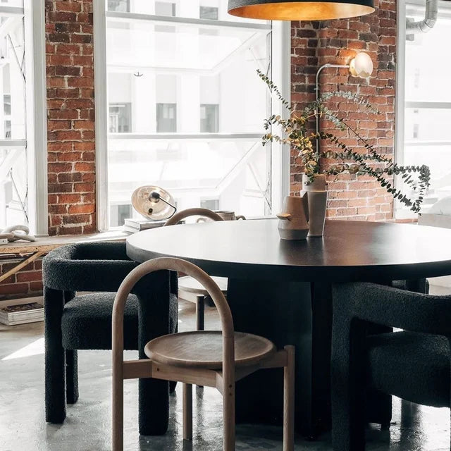 Modern dining area featuring Syrah Siyah Teddy Bukle chairs and a round black table with natural light and greenery.